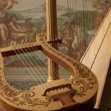 Starogrecki instrument strunowy, lirę, zdobią misternie wycięte wzory. Obok niej stoi harfa, tworząc muzyczną opowieść.