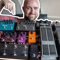 Uśmiechnięty mężczyzna pokazuje swoją bogatą kolekcję efektów gitarowych, prezentując ich kolejność na pedalboardzie.