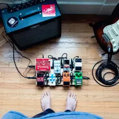Gitarzysta przygotowuje się do sesji, przed nim wzmacniacz, gitara i pedały efektów, w tym fuzz do gitary.