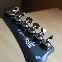 Czarna, matowa główka gitary do metalu z sześcioma kluczami strojeniowymi. Widoczny napis "buzz feiten TUNING SYSTEM".