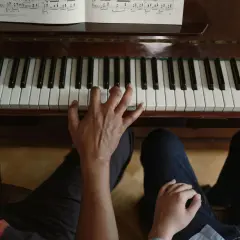 Dwie osoby grają na pianinie. Jedna ręka tworzy akompaniament, druga przygotowuje się do melodii.