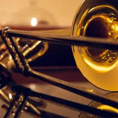 Błyszczący, złoty puzon z widocznym mechanizmem suwakowym. Instrument odbija się w gładkiej powierzchni, ukazując jego elegancki kształt.
