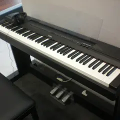 Czarny fortepian cyfrowy Yamaha P115 z klawiaturą, słuchawkami i trzema pedałami.