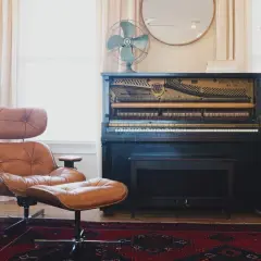 Strojenie pianina w salonie, obok skórzanego fotela i roślin.