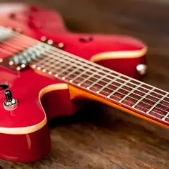 Czerwona gitara elektryczna leży na drewnianym blacie. Czy do gitary elektrycznej potrzebny jest wzmacniacz? Bez niego nie usłyszysz jej dźwięku.