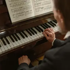 Dłonie muzyka grają melodię w tonacji **d dur** na fortepianie, nuty leżą otworem.