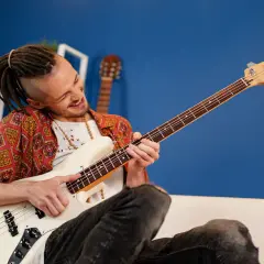 Mężczyzna z dredami gra na białej gitarze basowej typu semi hollow body, z pasją i uśmiechem.