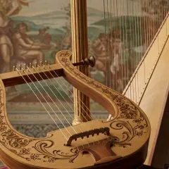 Starogrecki instrument strunowy, lirę, zdobią misternie wycięte wzory. Obok niej stoi harfa, tworząc muzyczną opowieść.