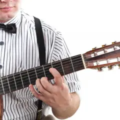 Mężczyzna w koszuli w paski i muszce gra na gitarze. Pokazuje, jak czytać tabulaturę, naciskając struny.