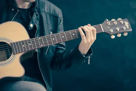 Mężczyzna w skórzanej kurtce gra na gitarze. Palce na gryfie tworzą akord, który brzmi jak początek rockowej ballady. Jaki to akord?