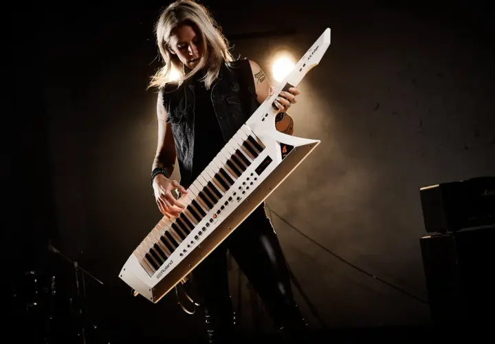 Kobieta gra na białym keyboardzie na pasku, który wygląda jak gitara.