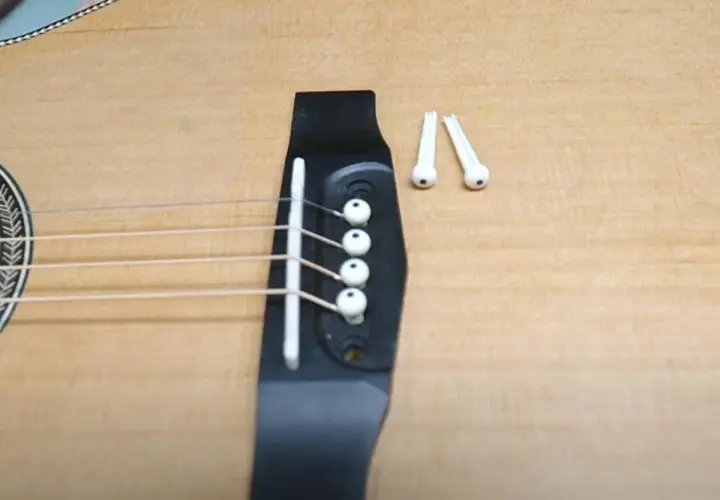 Gotowa do wymiany strun w gitarze akustycznej. Na mostku leżą nowe kołki.