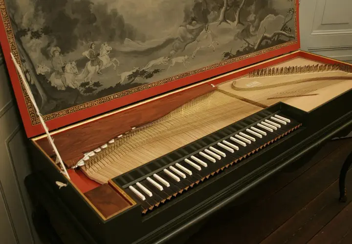 Stary klawikord z malowidłem przedstawiającym polowanie na koniach. Instrument z widocznymi strunami i klawiszami.