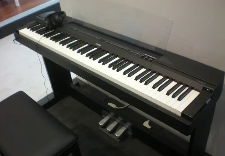 Czarny fortepian cyfrowy Yamaha P115 z klawiaturą, słuchawkami i trzema pedałami.