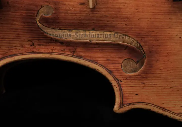 Fragment instrumentu Stradivarius z wygrawerowanym napisem. Drewno o ciepłym odcieniu, widoczne usłojenie.