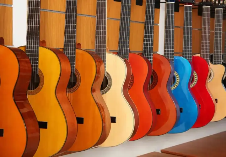 Rząd kolorowych gitar akustycznych, od pomarańczowej po czerwoną i niebieską, prezentuje różne rozmiary i odcienie.