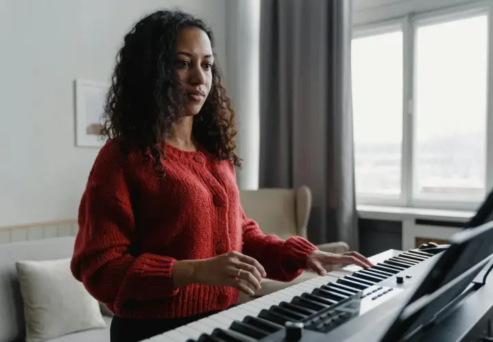Kobieta w czerwonym swetrze gra na keyboardzie, tworząc melodię w tonacji F dur.
