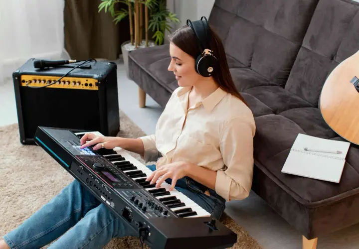 Kobieta w słuchawkach gra na keyboardzie japońskiej marki. Obok stoi wzmacniacz i gitara.