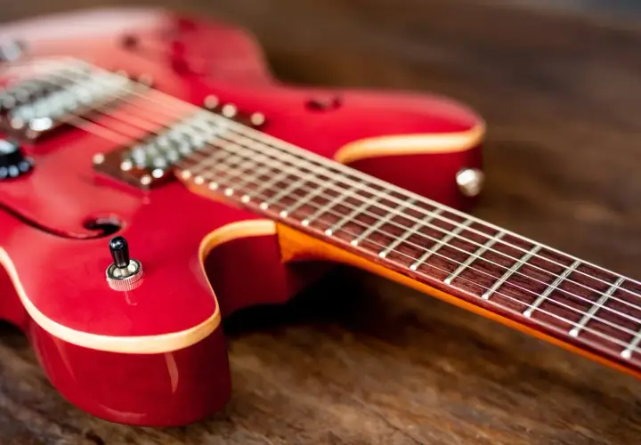 Czerwona gitara elektryczna leży na drewnianym blacie. Czy do gitary elektrycznej potrzebny jest wzmacniacz? Bez niego nie usłyszysz jej dźwięku.