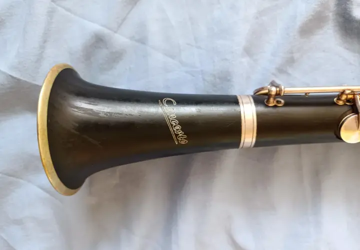 Część klarnetu z napisem "Concerto" i złotym pierścieniem. Widoczna jest budowa klarnetu, jego czarny korpus i metalowe klapy.