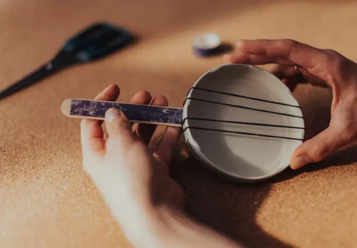 Ręce składają proste instrumenty muzyczne: talerzyk z gumkami i ozdobny patyczek.