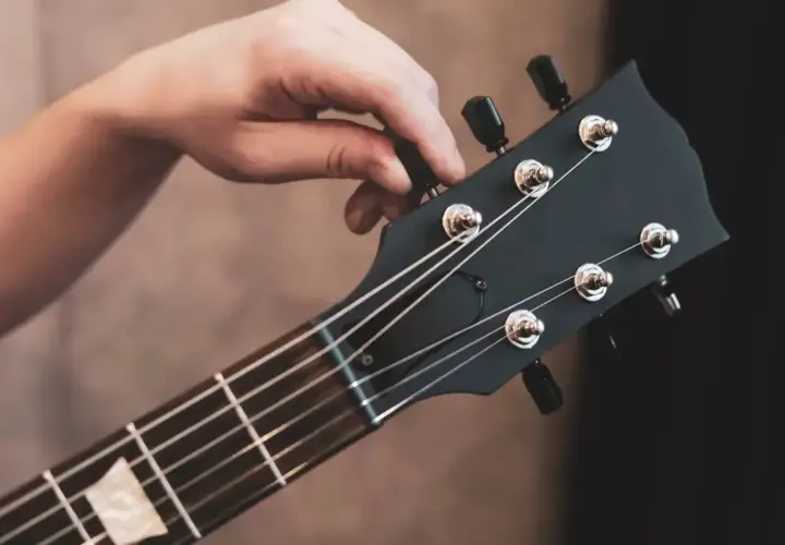 Dłoń kręci kluczem, strojąc gitarę. Słychać czysty dźwięk e, gotowy do gry.