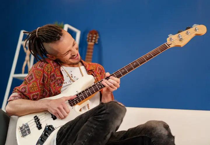 Mężczyzna z dredami gra na białej gitarze basowej typu semi hollow body, z pasją i uśmiechem.