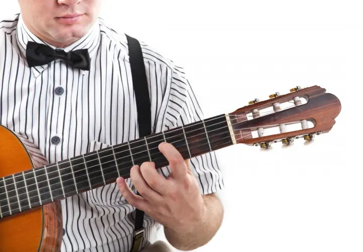 Mężczyzna w koszuli w paski i muszce gra na gitarze. Pokazuje, jak czytać tabulaturę, naciskając struny.