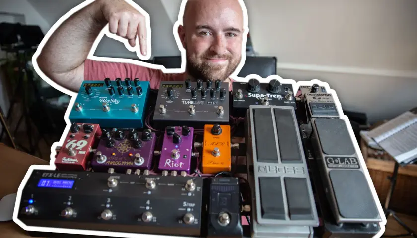 Uśmiechnięty mężczyzna pokazuje swoją bogatą kolekcję efektów gitarowych, prezentując ich kolejność na pedalboardzie.