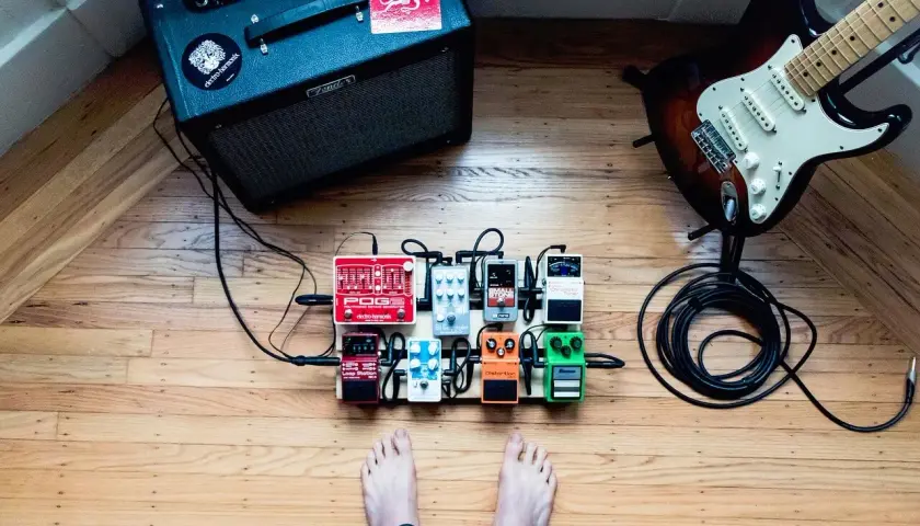 Gitarzysta przygotowuje się do sesji, przed nim wzmacniacz, gitara i pedały efektów, w tym fuzz do gitary.