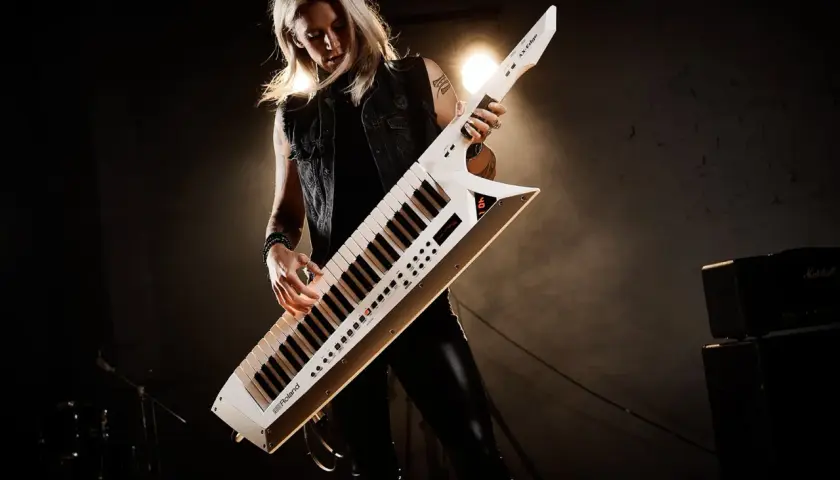 Kobieta gra na białym keyboardzie na pasku, który wygląda jak gitara.