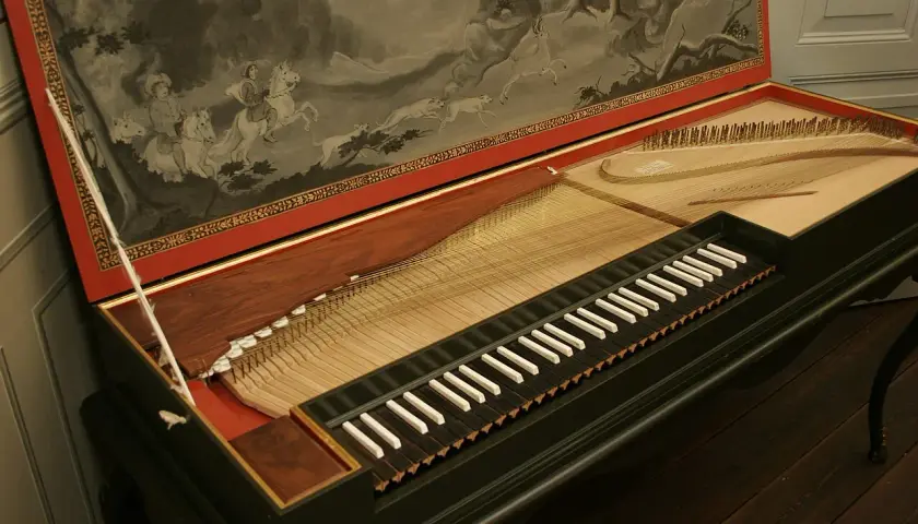 Stary klawikord z malowidłem przedstawiającym polowanie na koniach. Instrument z widocznymi strunami i klawiszami.