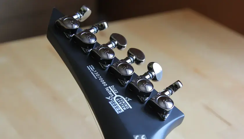 Czarna, matowa główka gitary do metalu z sześcioma kluczami strojeniowymi. Widoczny napis "buzz feiten TUNING SYSTEM".
