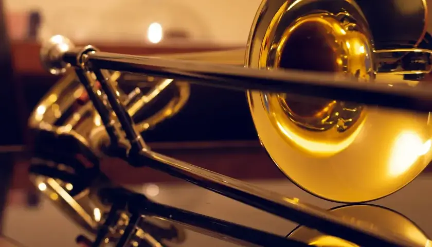 Błyszczący, złoty puzon z widocznym mechanizmem suwakowym. Instrument odbija się w gładkiej powierzchni, ukazując jego elegancki kształt.