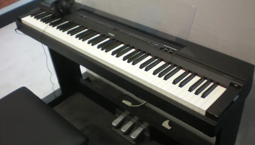 Czarny fortepian cyfrowy Yamaha P115 z klawiaturą, słuchawkami i trzema pedałami.