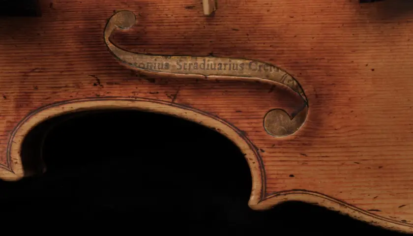 Fragment instrumentu Stradivarius z wygrawerowanym napisem. Drewno o ciepłym odcieniu, widoczne usłojenie.