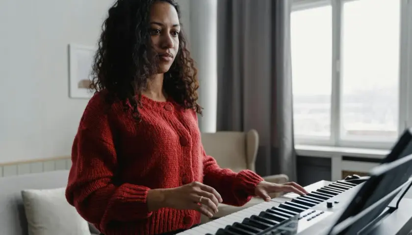 Kobieta w czerwonym swetrze gra na keyboardzie, tworząc melodię w tonacji F dur.