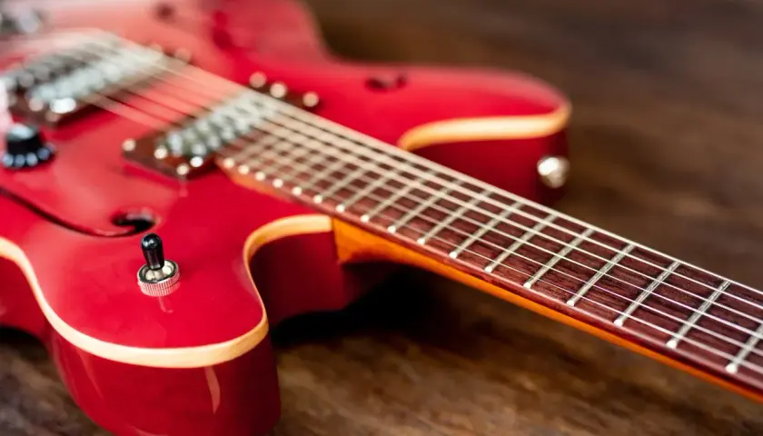 Czerwona gitara elektryczna leży na drewnianym blacie. Czy do gitary elektrycznej potrzebny jest wzmacniacz? Bez niego nie usłyszysz jej dźwięku.