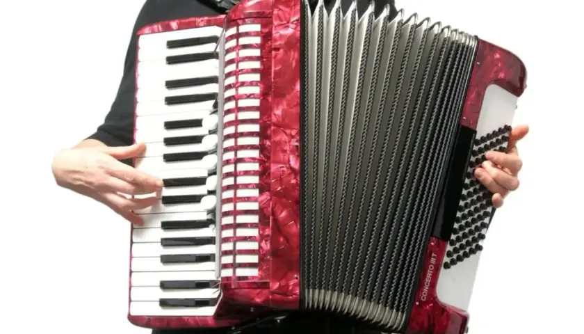 Ręce grają na czerwonym akordeonie. Widoczna klawiatura i miech, ukazujące budowę instrumentu.