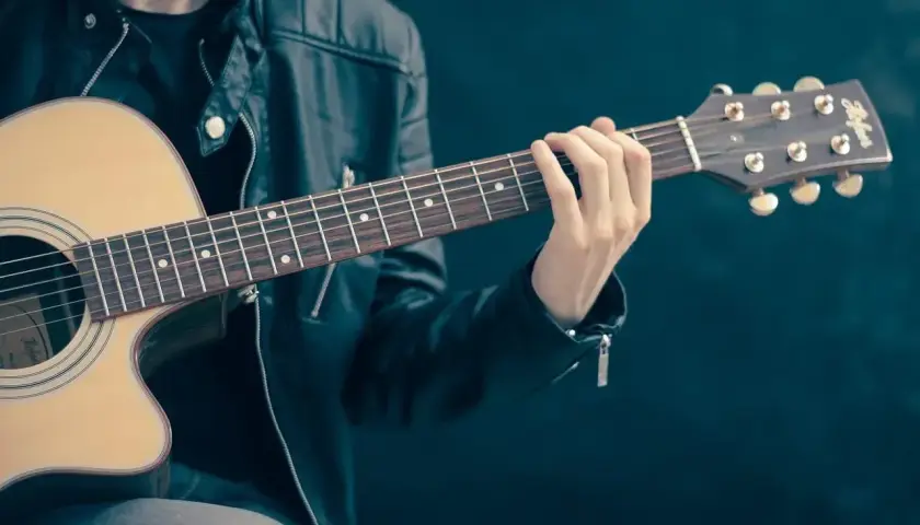 Mężczyzna w skórzanej kurtce gra na gitarze. Palce na gryfie tworzą akord, który brzmi jak początek rockowej ballady. Jaki to akord?