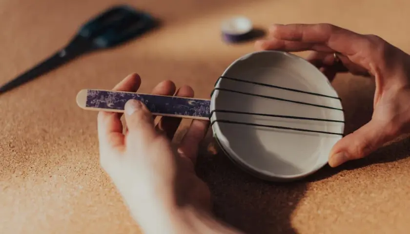 Ręce składają proste instrumenty muzyczne: talerzyk z gumkami i ozdobny patyczek.