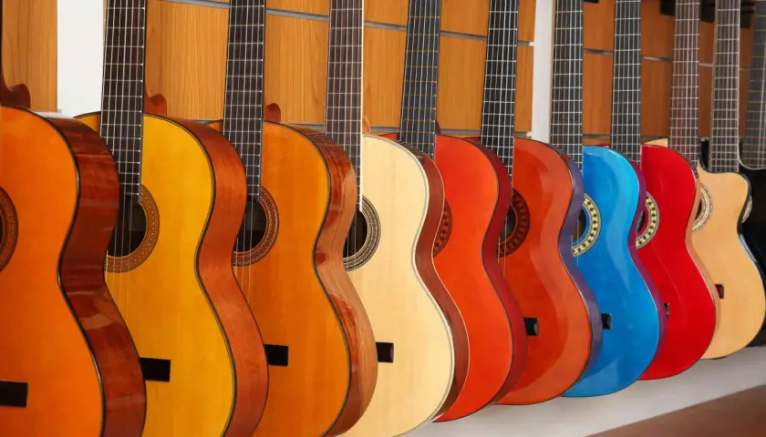 Rząd gitar klasycznych i akustycznych w różnych kolorach. Różnice między nimi to m.in. struny i pudło rezonansowe.