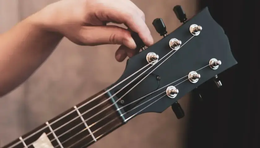 Dłoń kręci kluczem, strojąc gitarę. Słychać czysty dźwięk e, gotowy do gry.