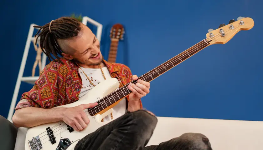 Mężczyzna z dredami gra na białej gitarze basowej typu semi hollow body, z pasją i uśmiechem.
