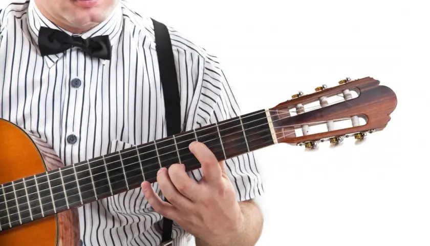 Mężczyzna w koszuli w paski i muszce gra na gitarze. Pokazuje, jak czytać tabulaturę, naciskając struny.