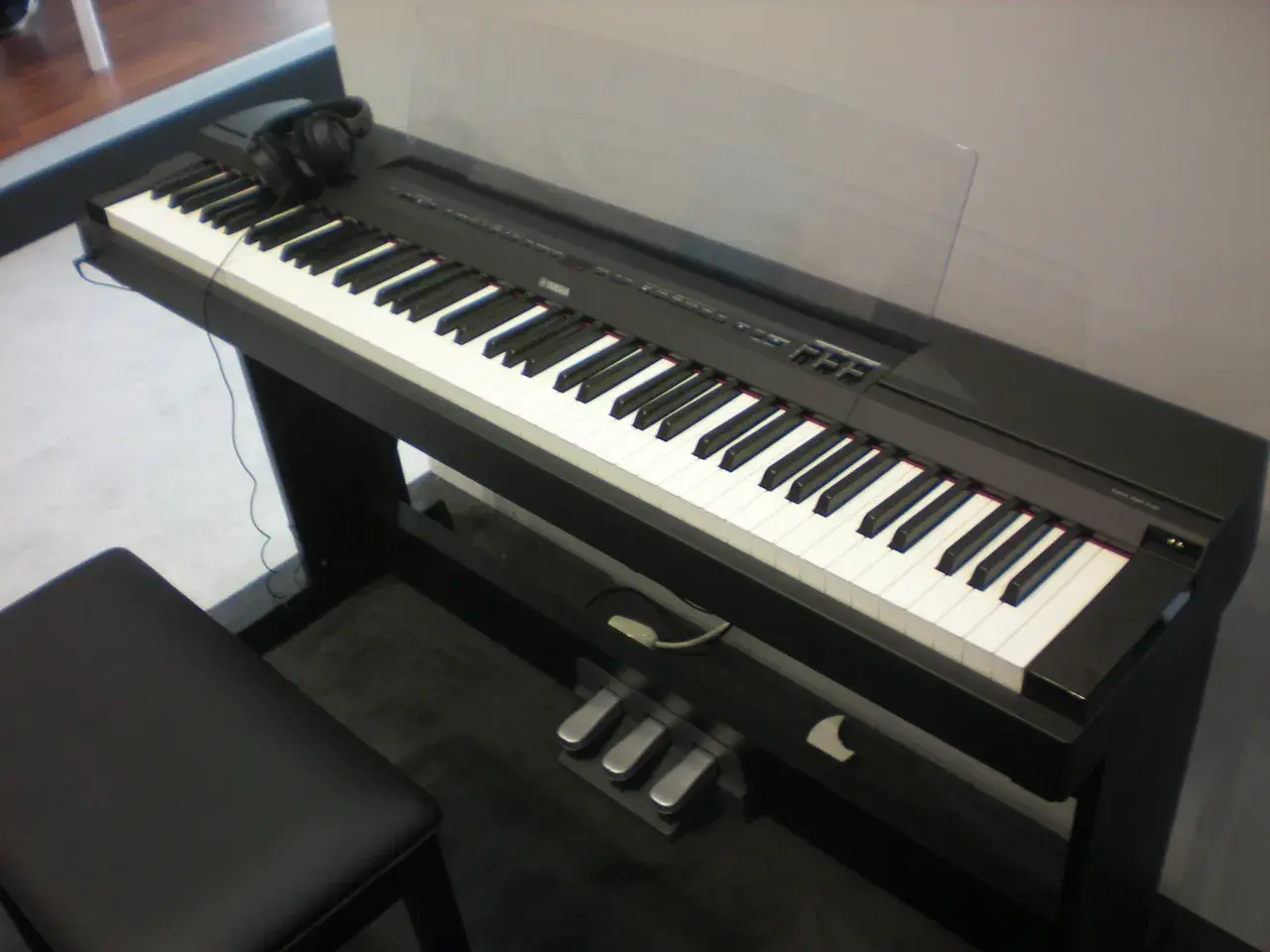 Czarny fortepian cyfrowy Yamaha P115 z klawiaturą, słuchawkami i trzema pedałami.