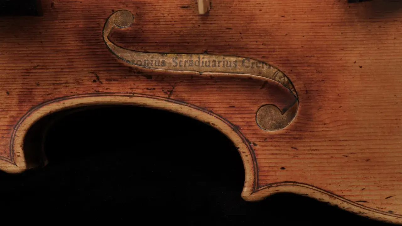 Fragment instrumentu Stradivarius z wygrawerowanym napisem. Drewno o ciepłym odcieniu, widoczne usłojenie.