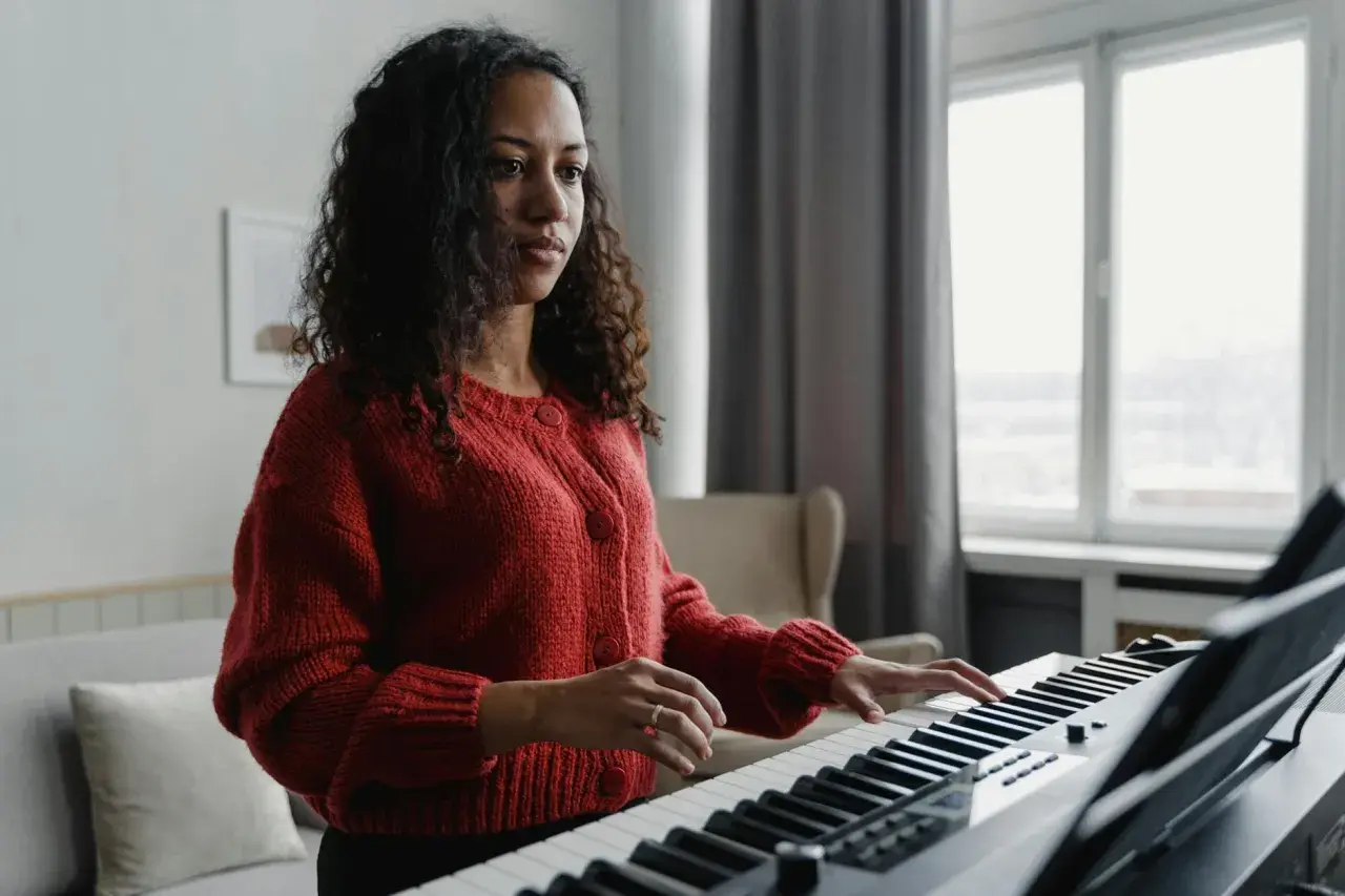 Kobieta w czerwonym swetrze gra na keyboardzie, tworząc melodię w tonacji F dur.