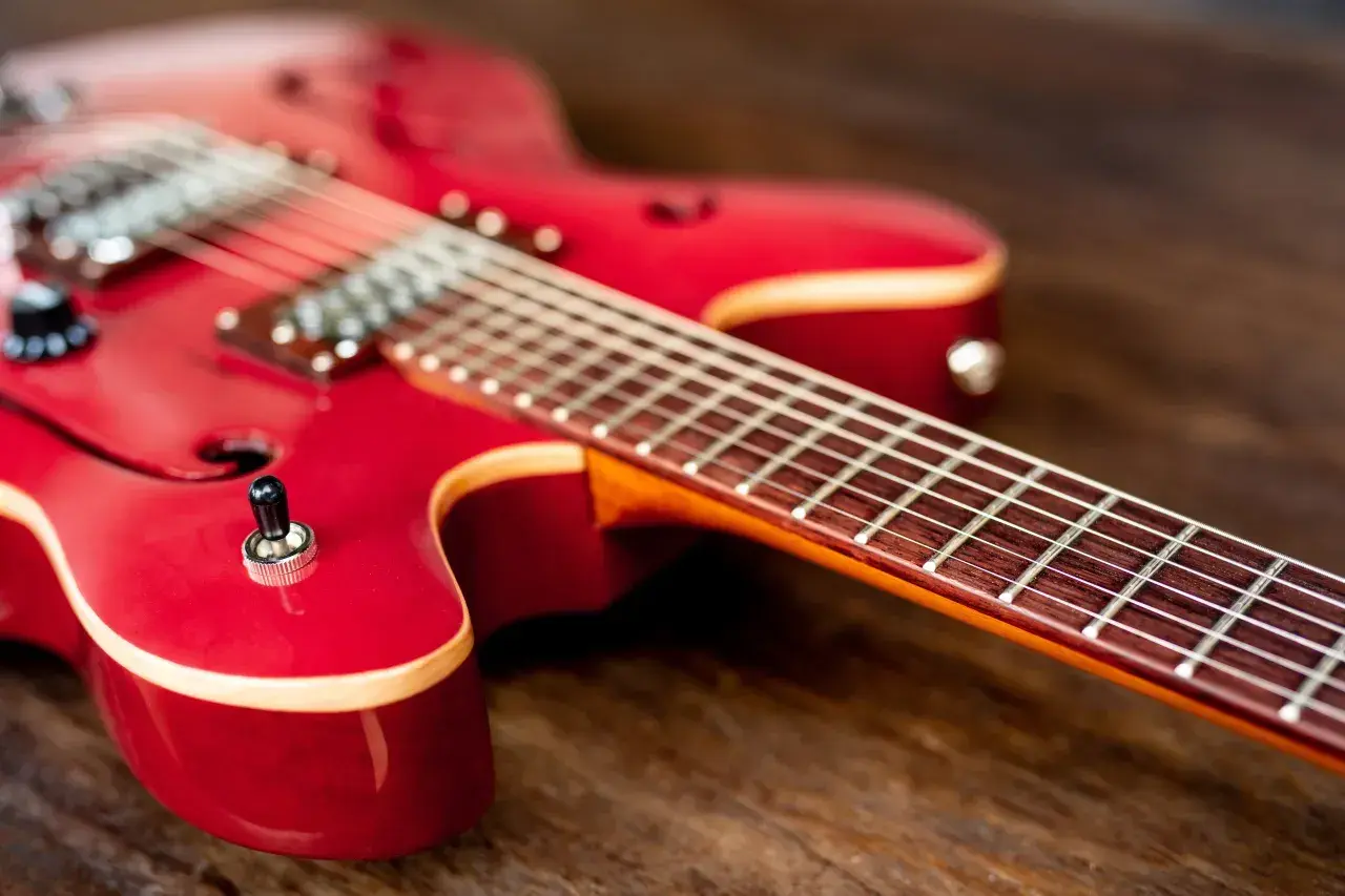 Czerwona gitara elektryczna leży na drewnianym blacie. Czy do gitary elektrycznej potrzebny jest wzmacniacz? Bez niego nie usłyszysz jej dźwięku.