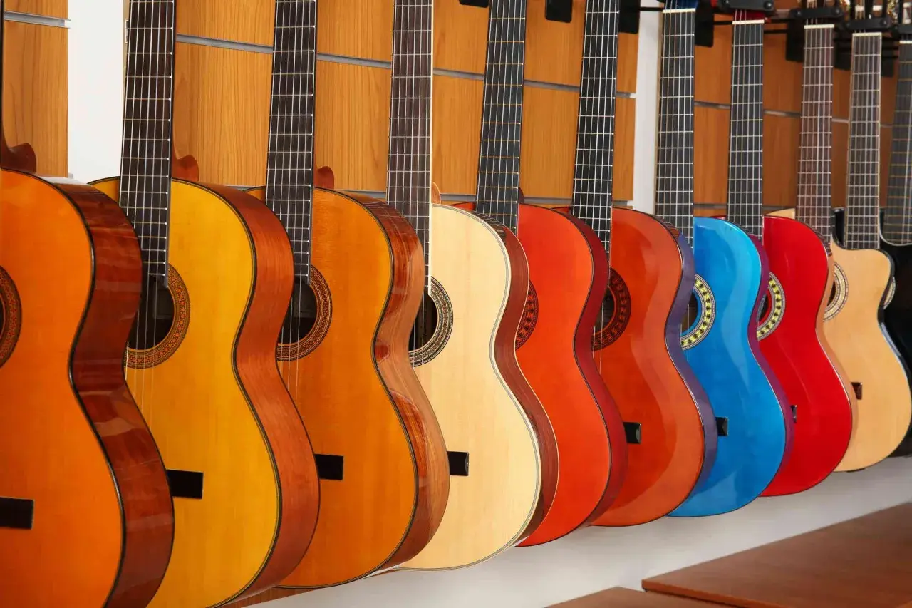 Rząd gitar klasycznych i akustycznych w różnych kolorach. Różnice między nimi to m.in. struny i pudło rezonansowe.